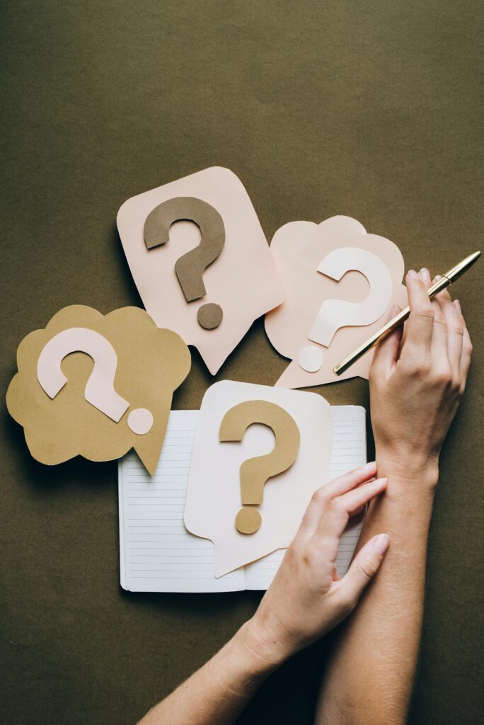 pexels-photo-5428833-5428833 Hands holding pen next to paper question marks on notebook, symbolizing inquiry and creativity.